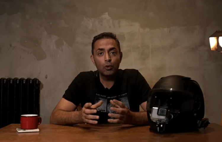 A man speaks to the camera at a desk.